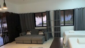 A modern room with a grey sofa, a small table, two beds, and large windows with curtains. - Crystal Cove (Sipalay)