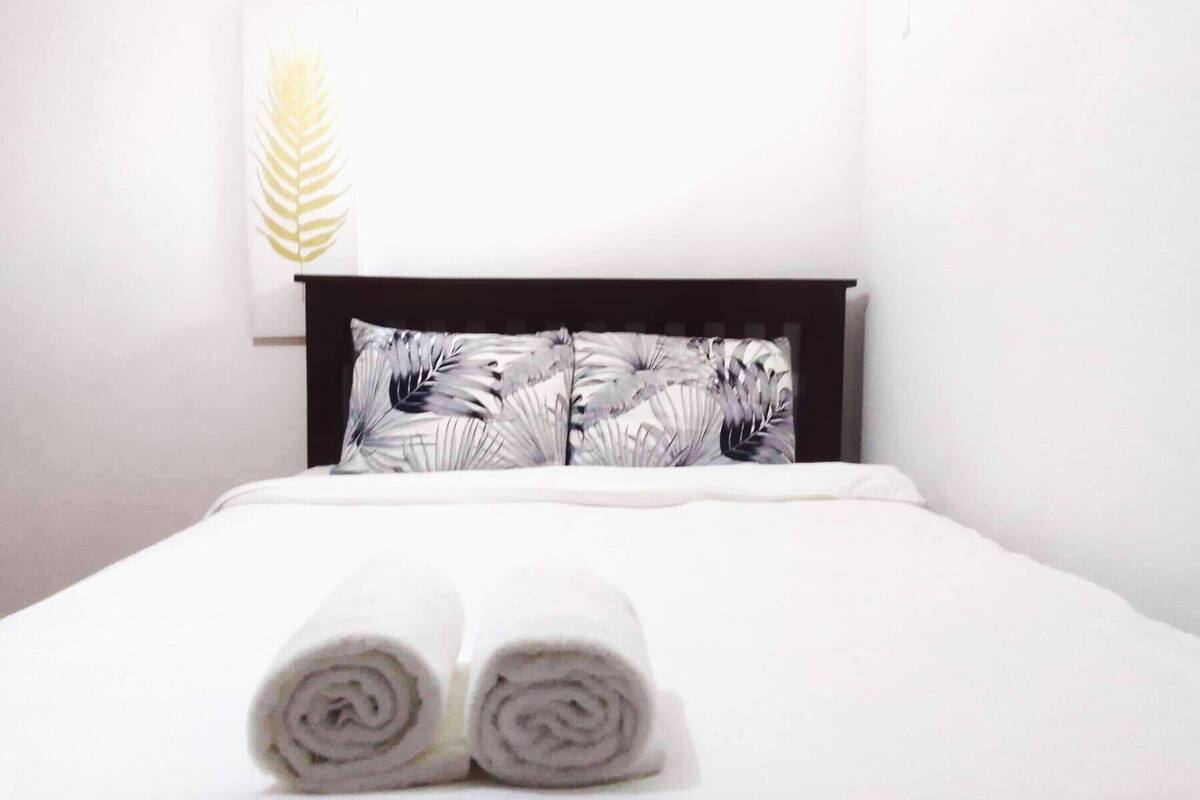 Una cama bien hecha con toallas enrolladas, un cabecero oscuro y una obra de arte colgada en la pared.