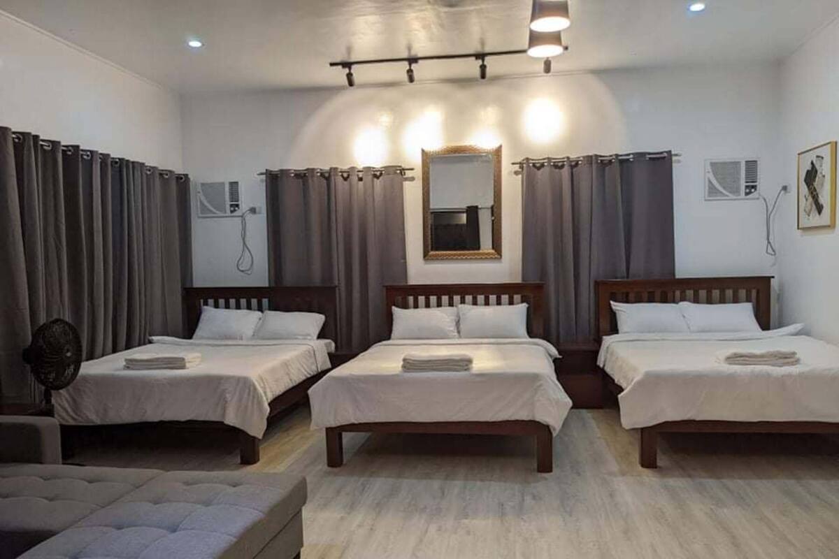Habitación de hotel con tres camas individuales, un espejo grande y un sofá.