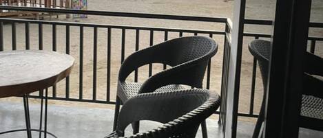 A beachside patio with wicker chairs and a table, overlooking the sea and a mountain.