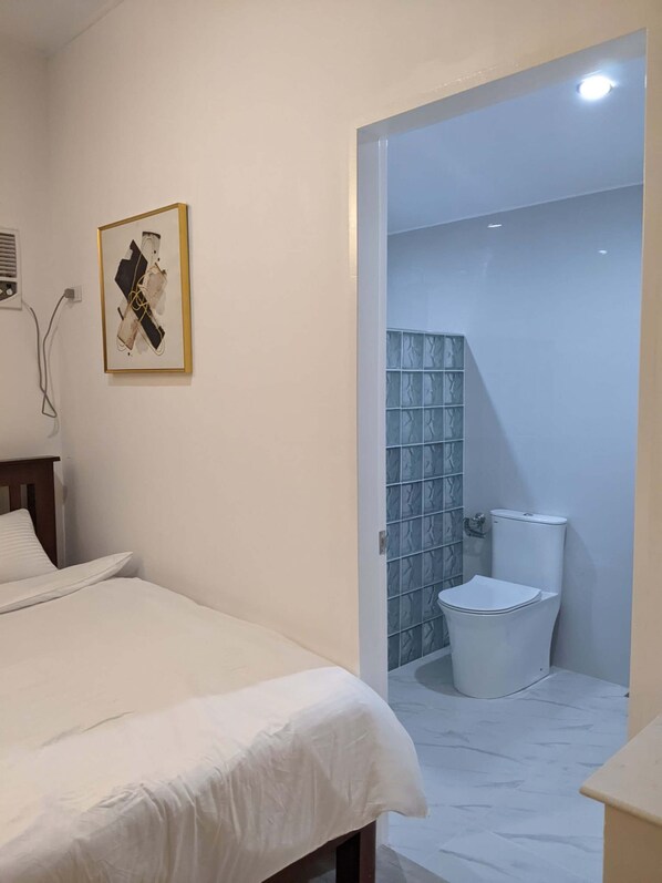 A hotel room with a bed, a framed artwork on the wall, and a bathroom with a toilet and tiled walls.