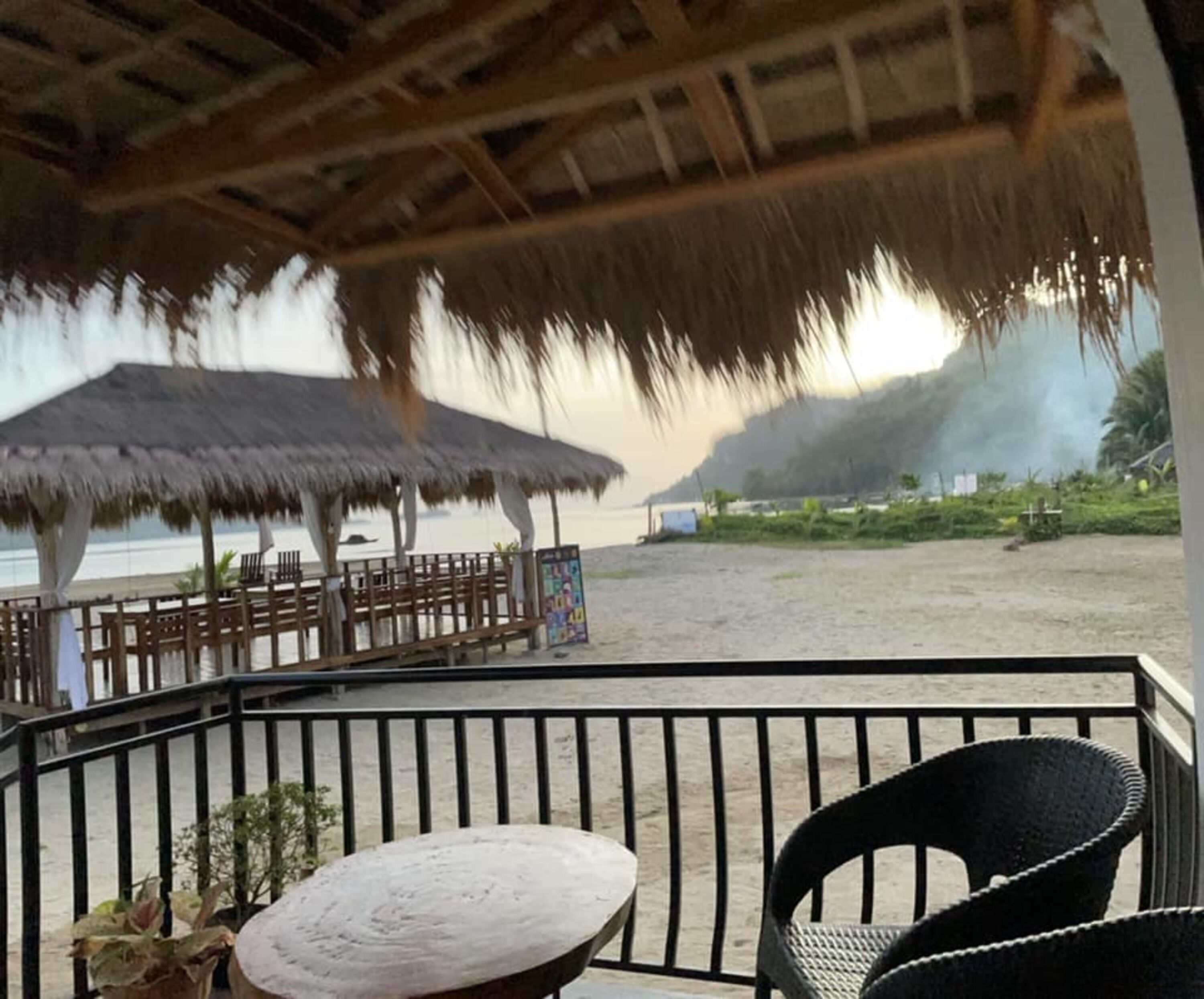 Un restaurante frente al mar con techo de paja, mesas al aire libre y vista a la playa.