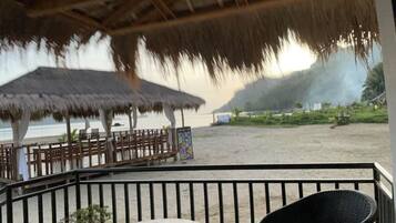 Un restaurante frente al mar con techo de paja, mesas al aire libre y vista a la playa.