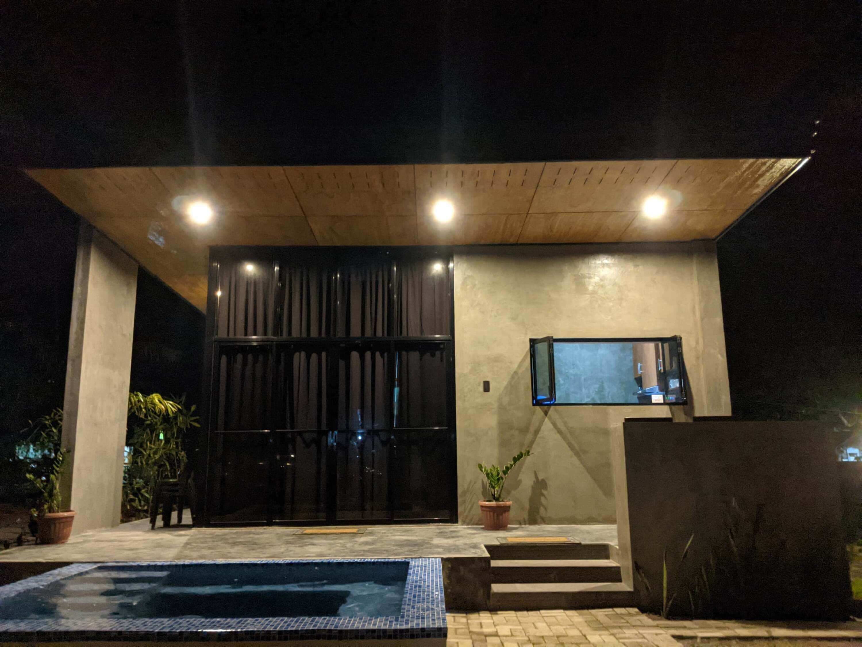 Un edificio moderno con un gran portón negro, una piscina pequeña y una planta en maceta.