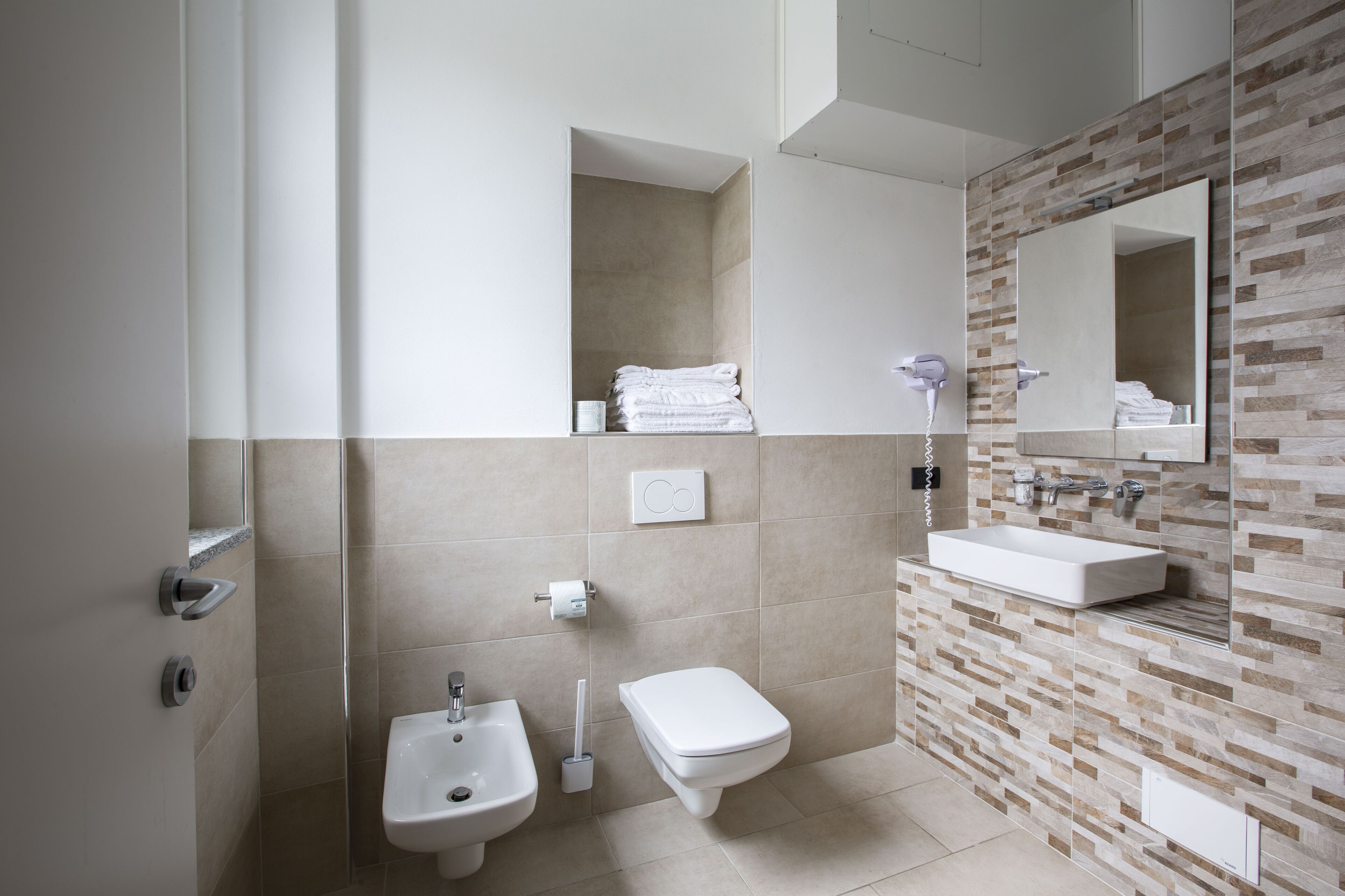 A modern bathroom with a bidet, toilet, sink, and a mirror with a tile backsplash.