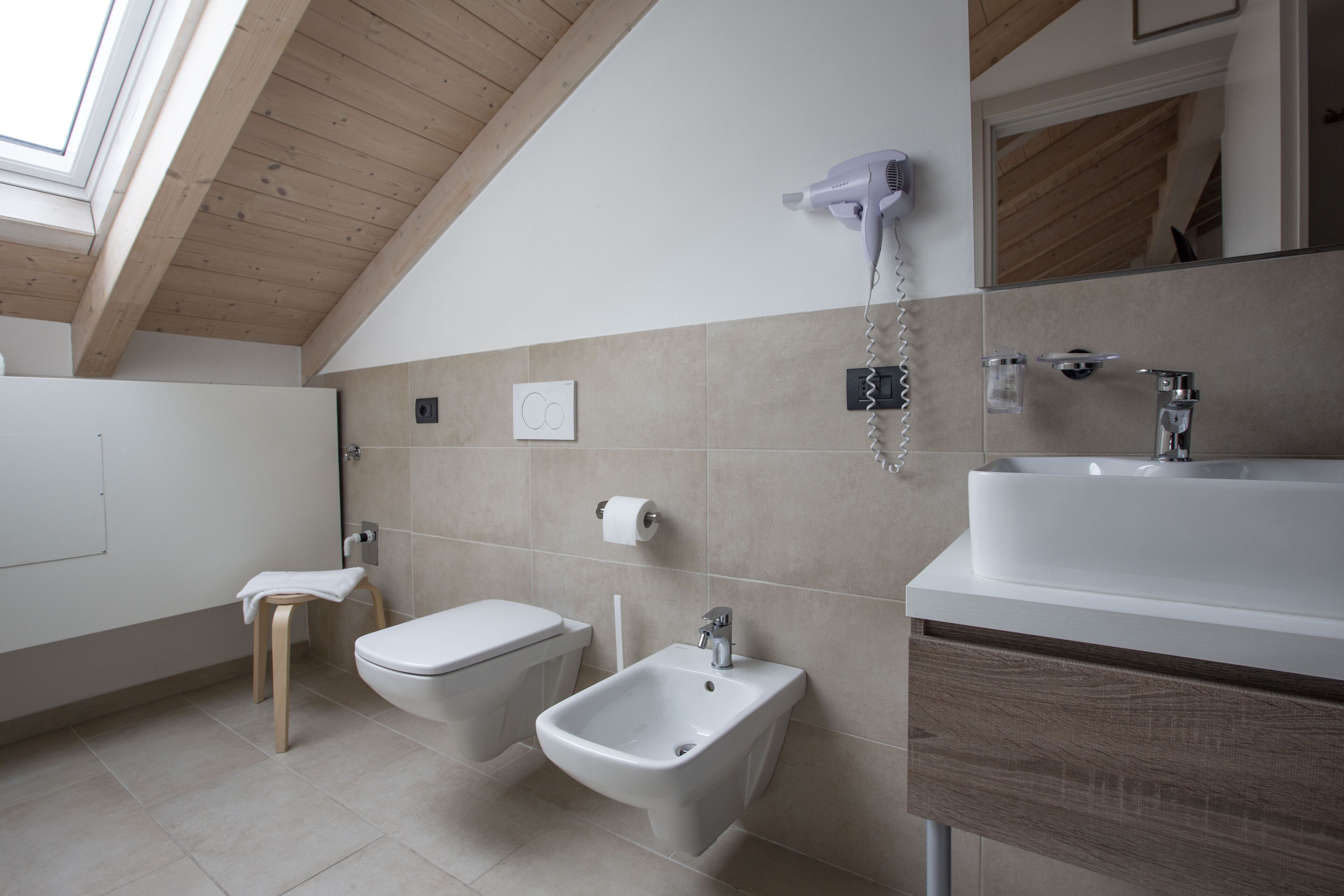 Een moderne badkamer met een bidet, toilet, wastafel en een aan de muur bevestigde haardroger.