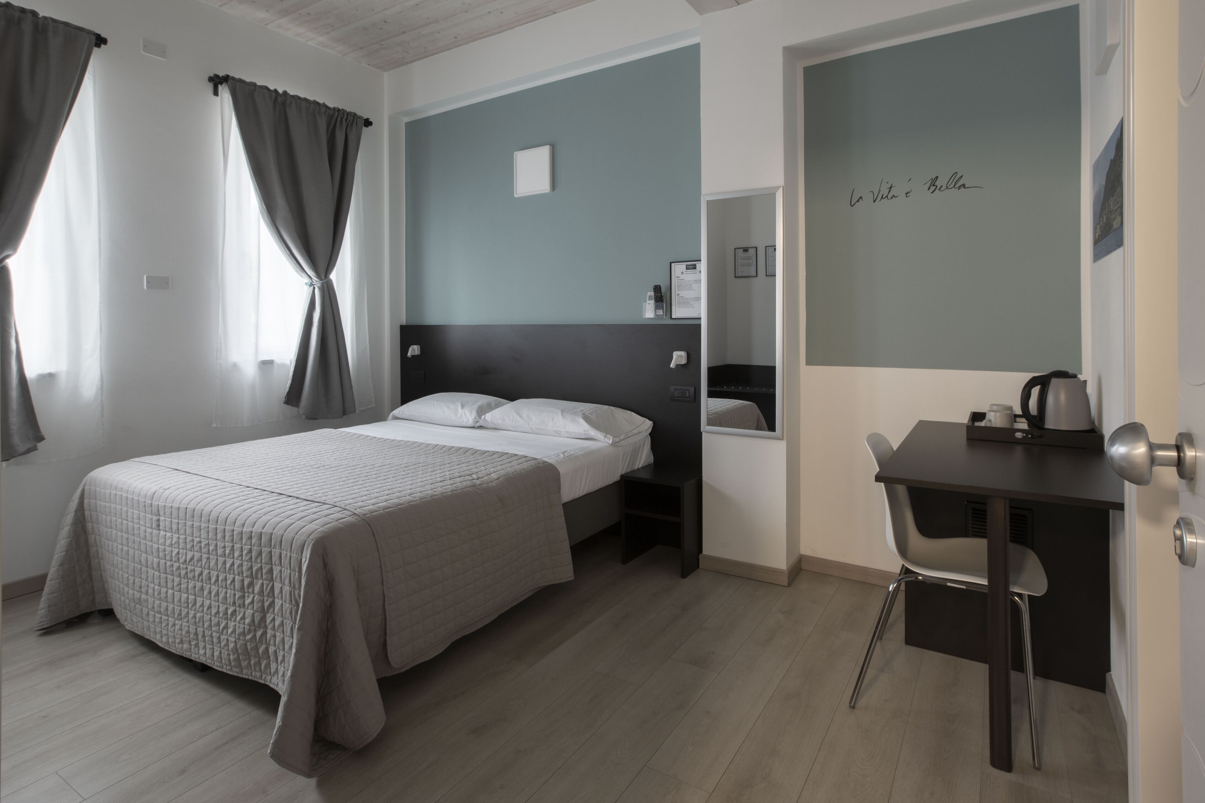 A bedroom with a bed, a desk, and a chair. There is a wall with a framed picture and a sign.