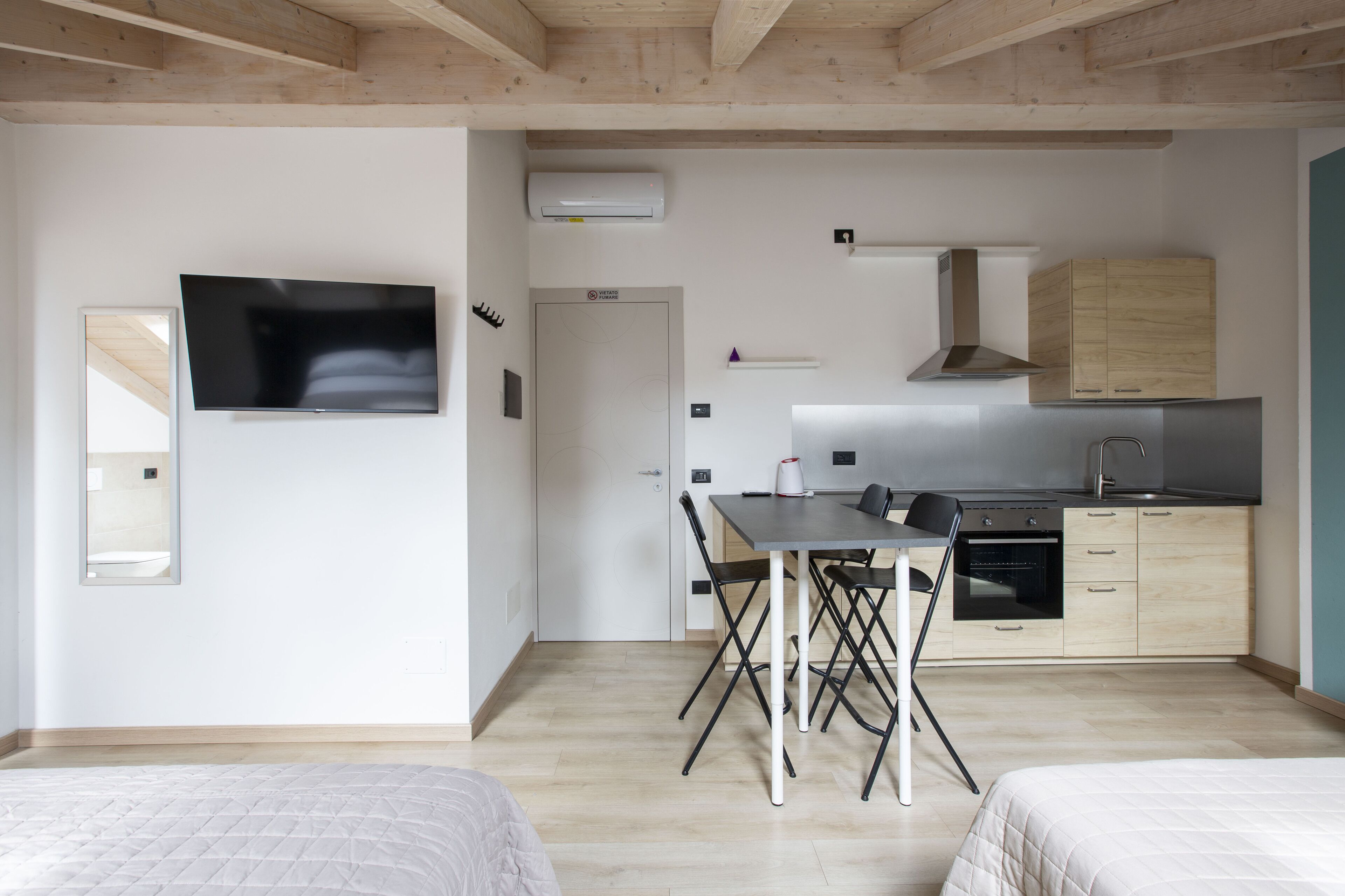 Un espace de vie moderne et compact, comprenant un coin cuisine, un espace repas avec une table et des chaises, et un téléviseur fixé au mur.