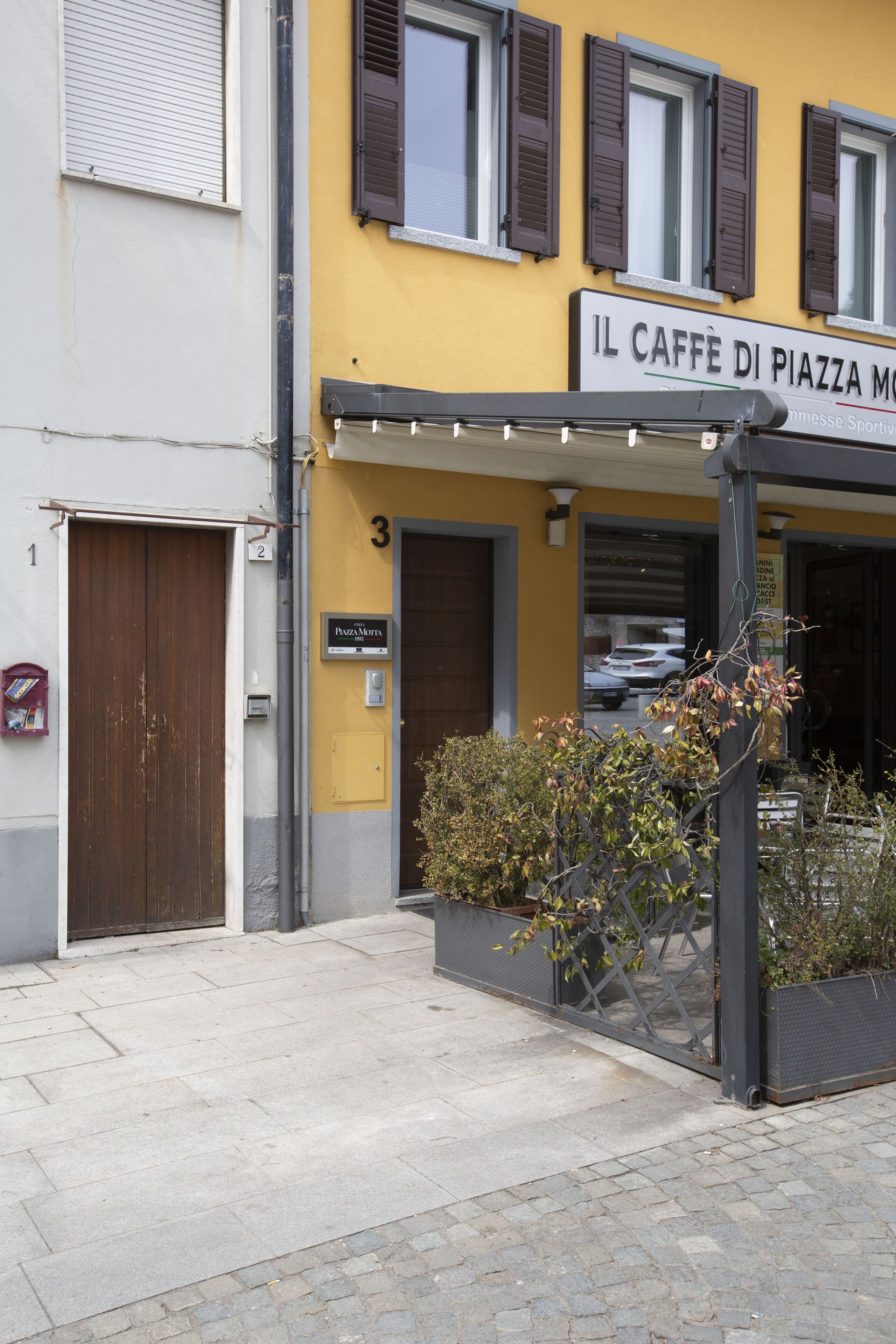Un edificio con un cartello che riporta "IL CAFFÈ DI PIAZZA M" e il numero "3" sulla porta.