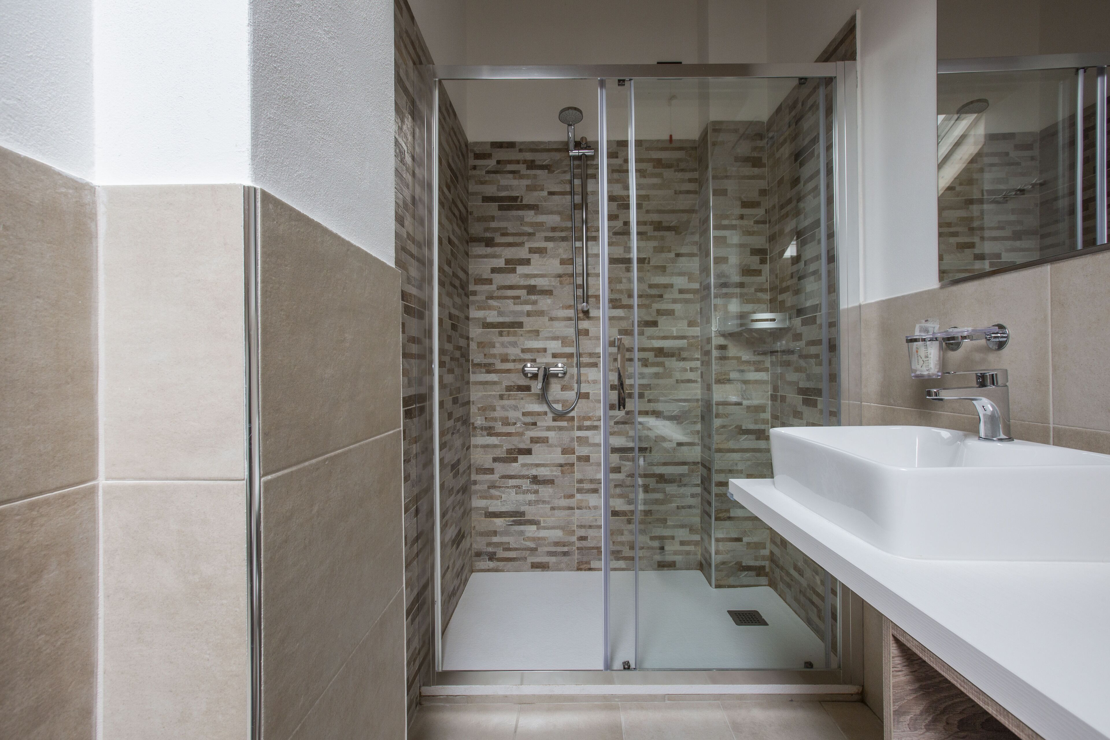 Un bagno moderno con cabina doccia in vetro, lavandino bianco e schienale piastrellato.