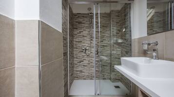 Un bagno moderno con cabina doccia in vetro, lavandino bianco e schienale piastrellato.