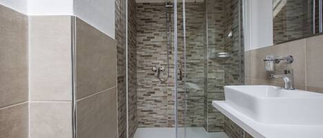 Un baño moderno con ducha envuelta en vidrio, un lavabo blanco y un salpicadero de azulejos.