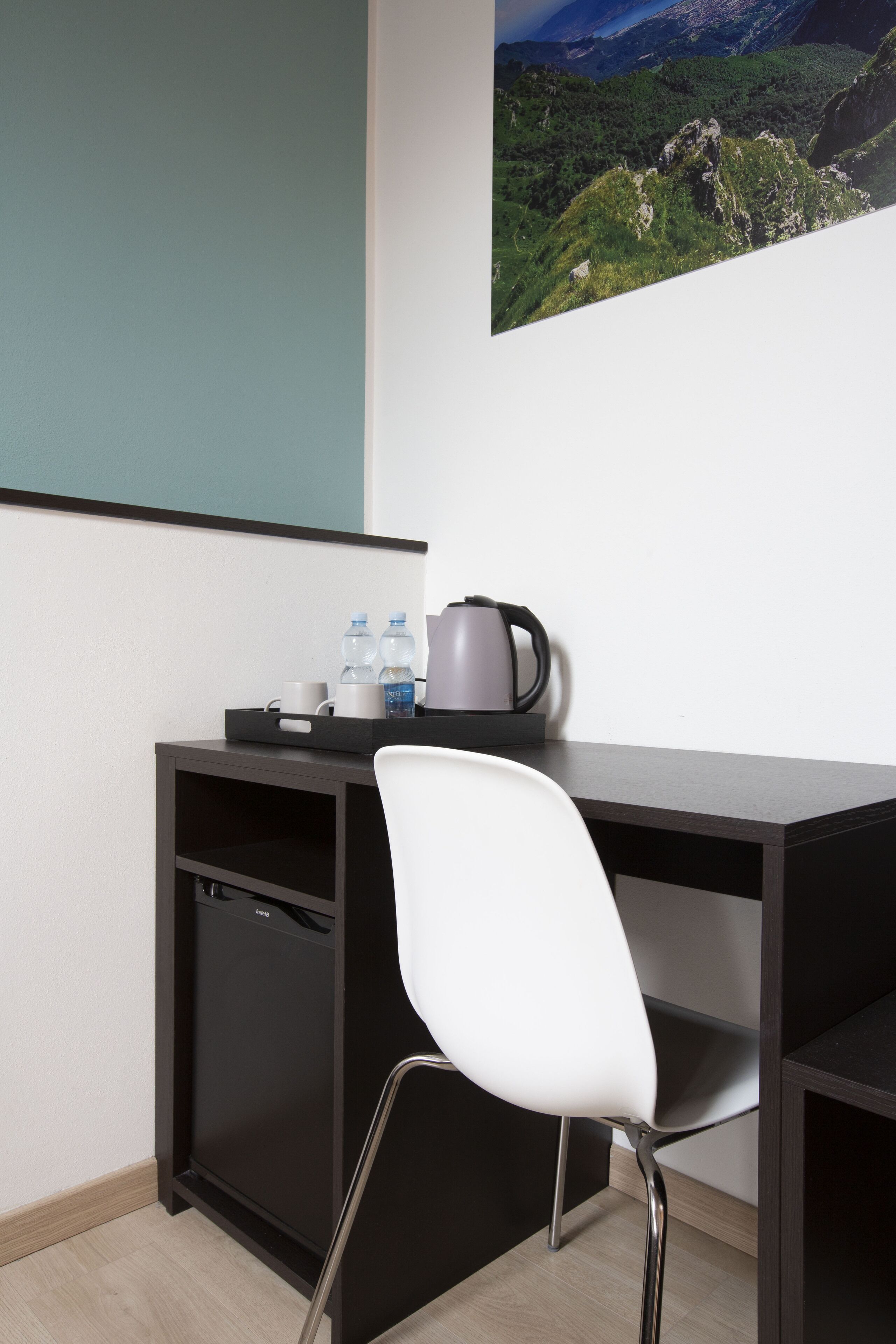 A modern office desk with a white chair, a black coffee maker, and two water bottles on a tray.