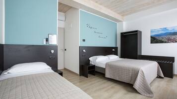 Une chambre d’hôtel avec deux lits, une armoire noire, un mur orné d’un tableau représentant un paysage urbain, et un mur d’accent de couleur turquoise sur lequel sont inscrites des citations inspirantes.