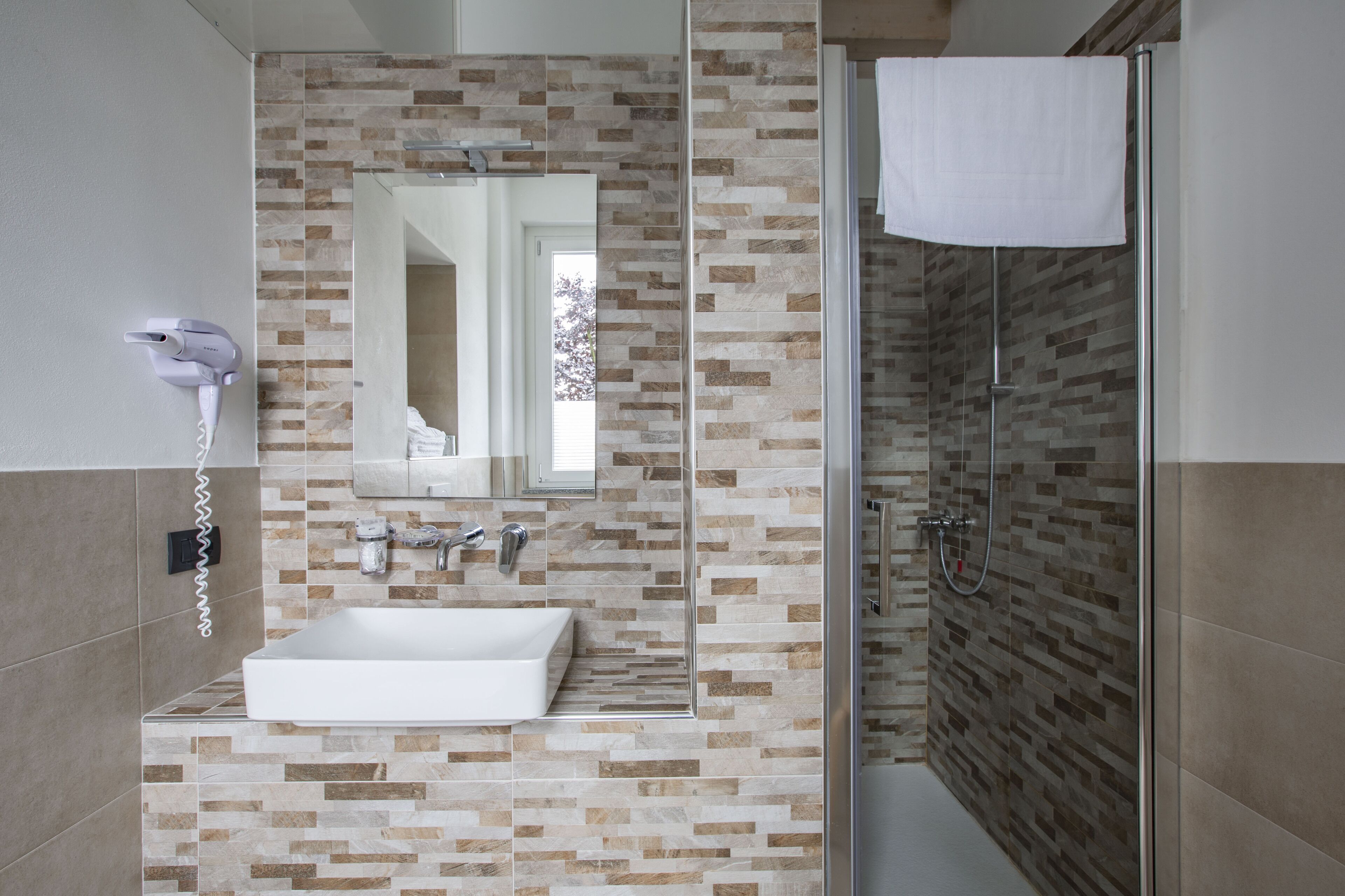 A modern bathroom with a rectangular sink, a mirror, a hairdryer, and a shower with a glass door.