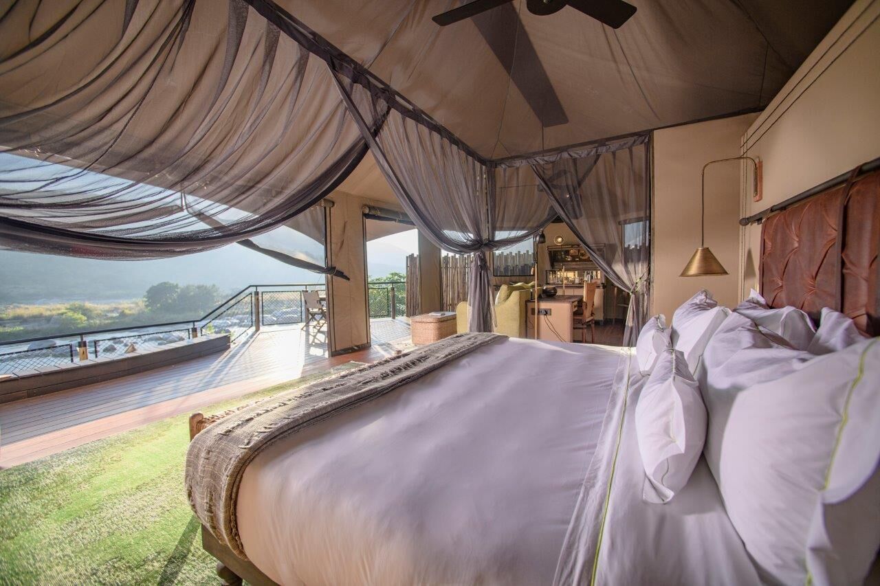 A bedroom with a large bed, a balcony with a view, and a ceiling fan.