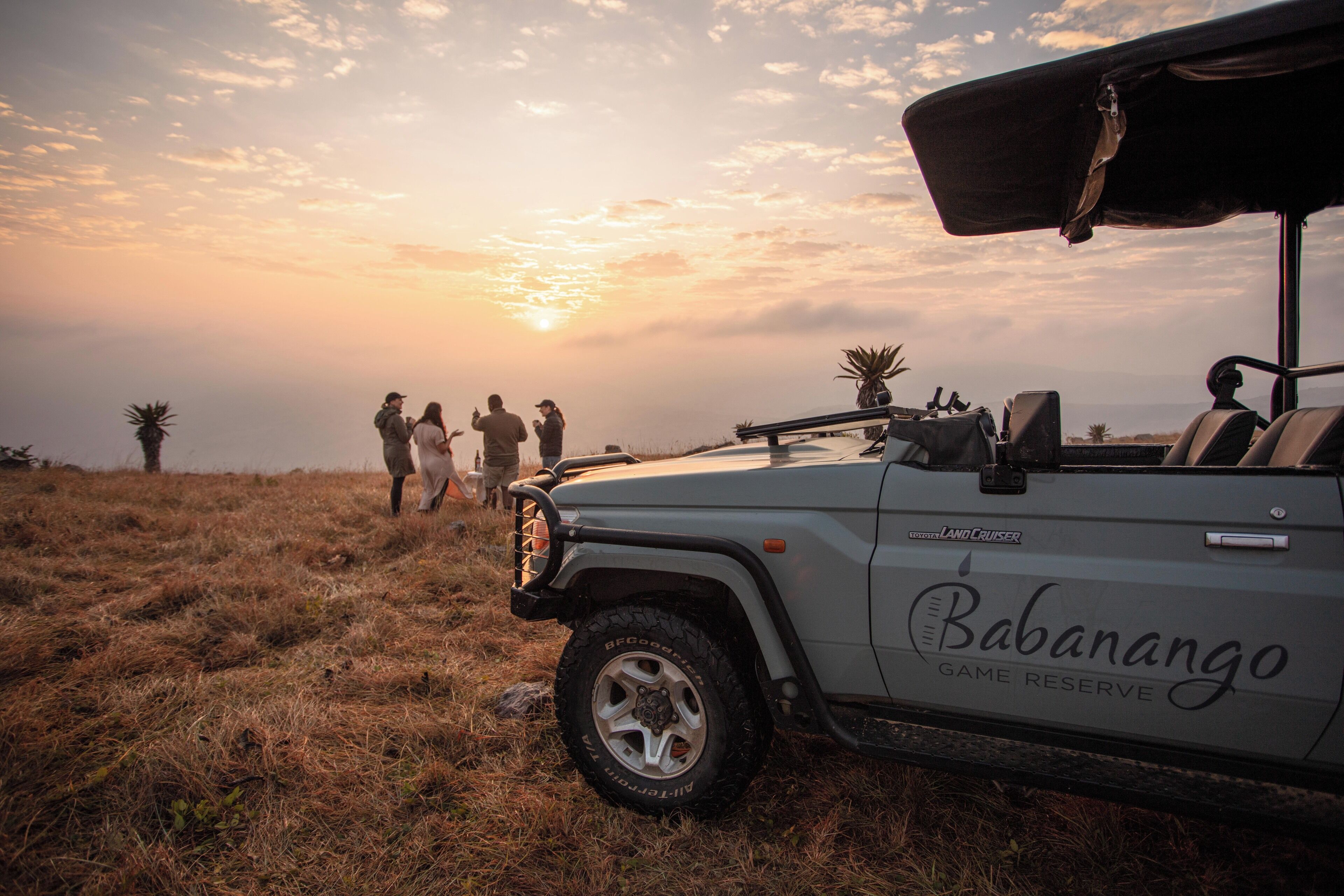 A safari vehicle with "Babanango Game Reserve" written on the side parked on a grassy field.