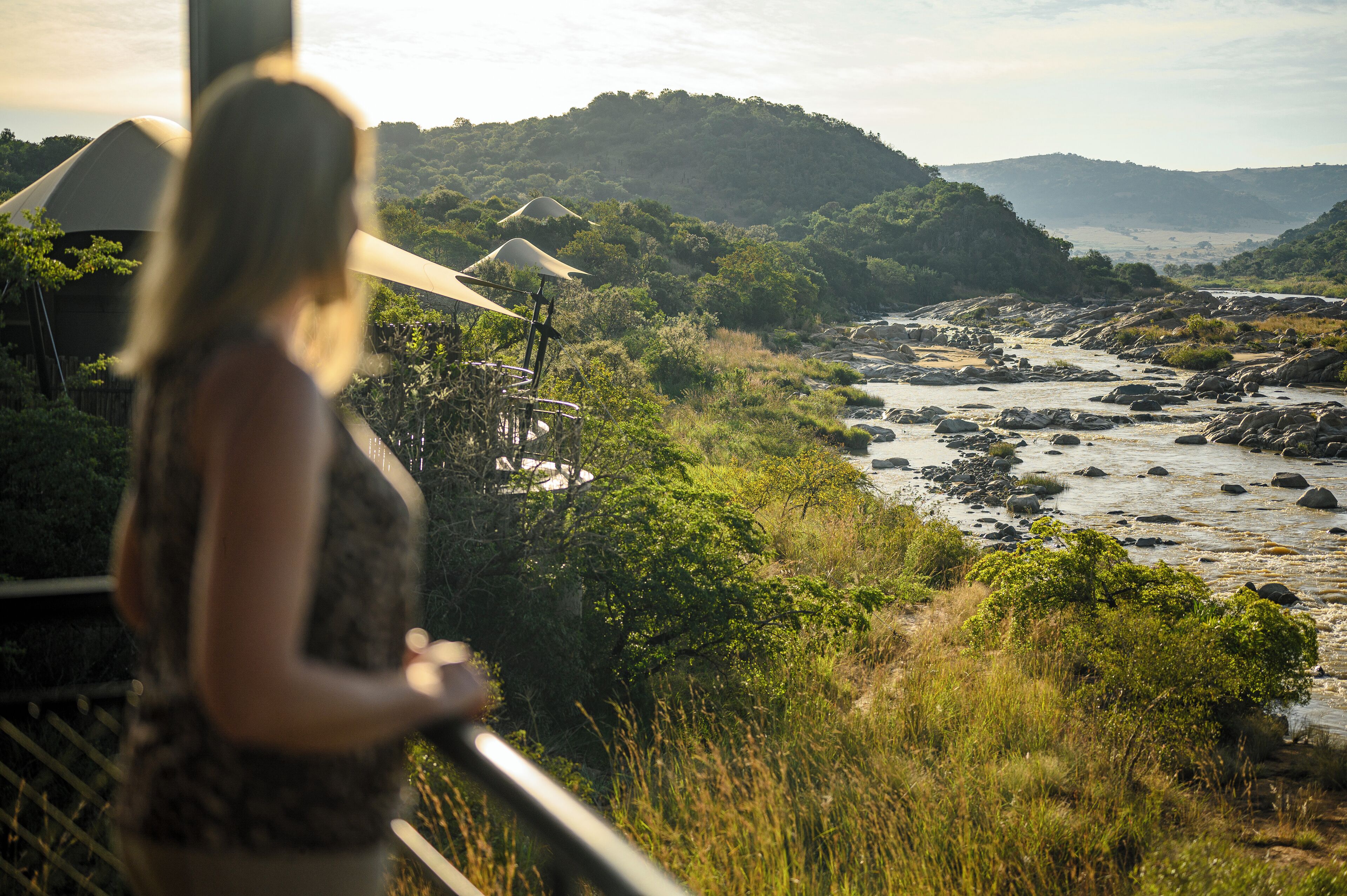 A woman overlooking a river with surrounding greenery and hills.