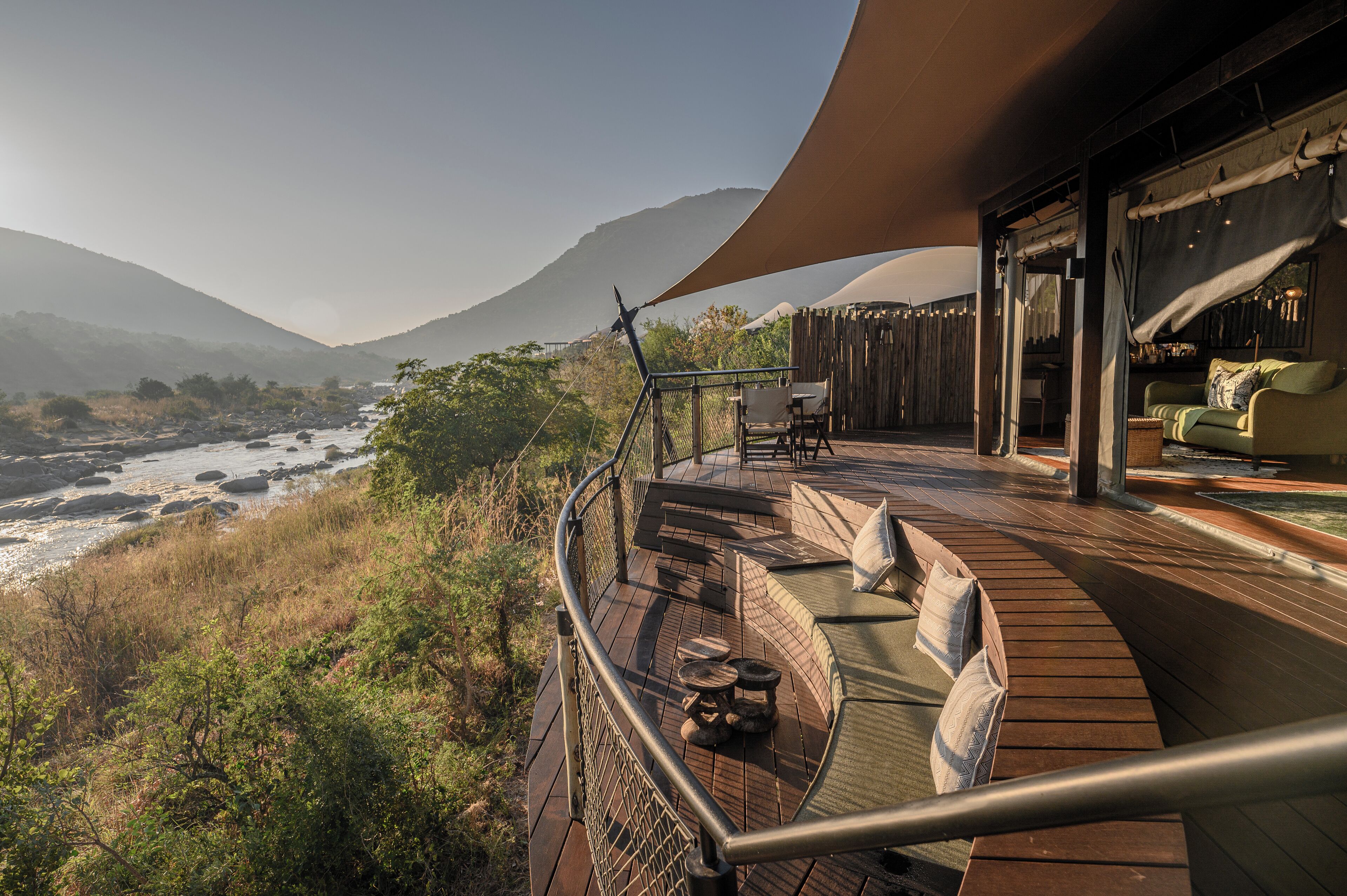 Una terraza con mobiliario exterior que da a un río y montañas.