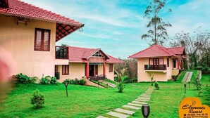 A resort with two buildings, each with a red-tiled roof and a small porch. There is a well-maintained lawn and a stone pathway leading to the buildings. - Elements Resort (Mananthavady)