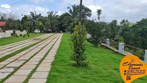 A pathway leading to a resort with a well-maintained lawn and palm trees. - Elements Resort (Mananthavady)