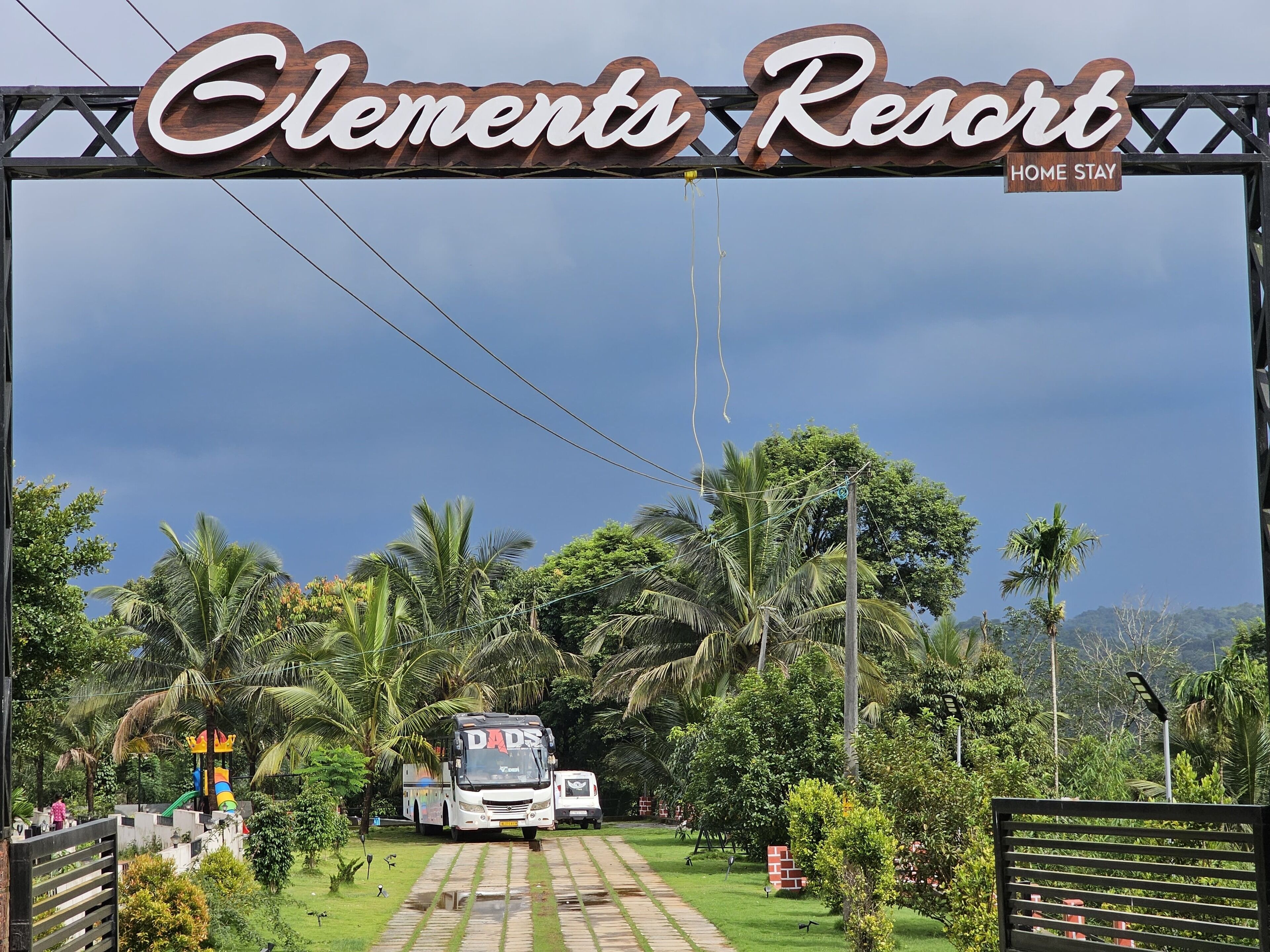 A sign for Elements Resort with a pathway leading to a bus and a playground.