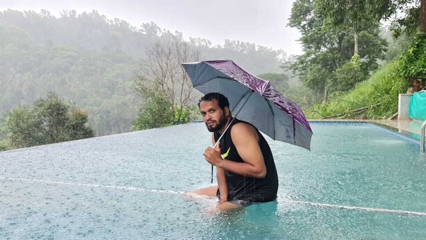 A person sitting on the edge of a pool with a purple umbrella, surrounded by a lush, forested hillside. - Elements Resort (Mananthavady)