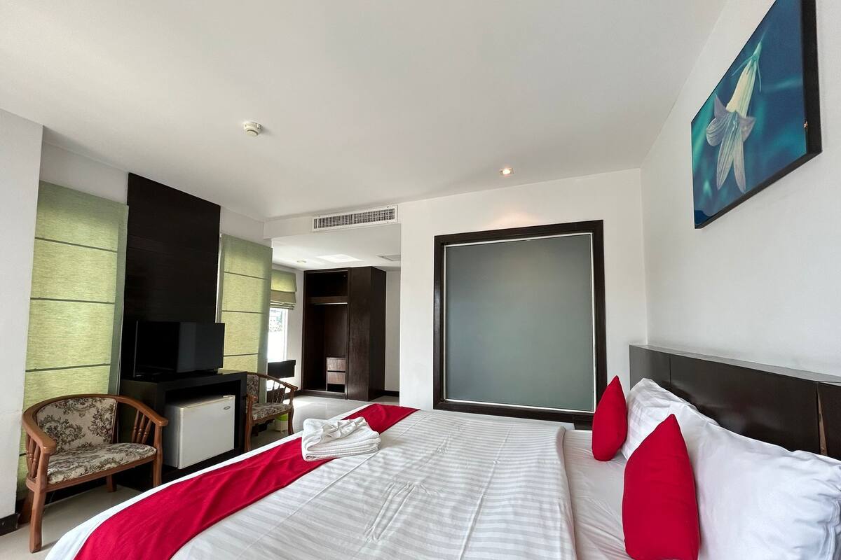 Une chambre d’hôtel avec un grand lit, une télévision, un bureau avec une chaise et une grande fenêtre.