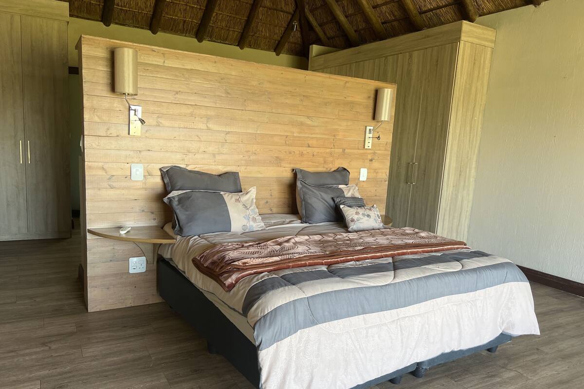 A bedroom with a wooden headboard, a bed with multiple pillows, a bedside table, and a nightstand.