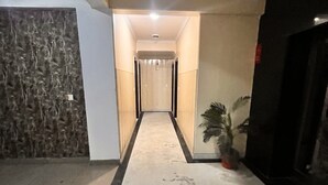 A hallway with a marble floor, a ceiling fan, and a plant on the right. - HOTEL GRAND HIGHWAY (Faridabad)