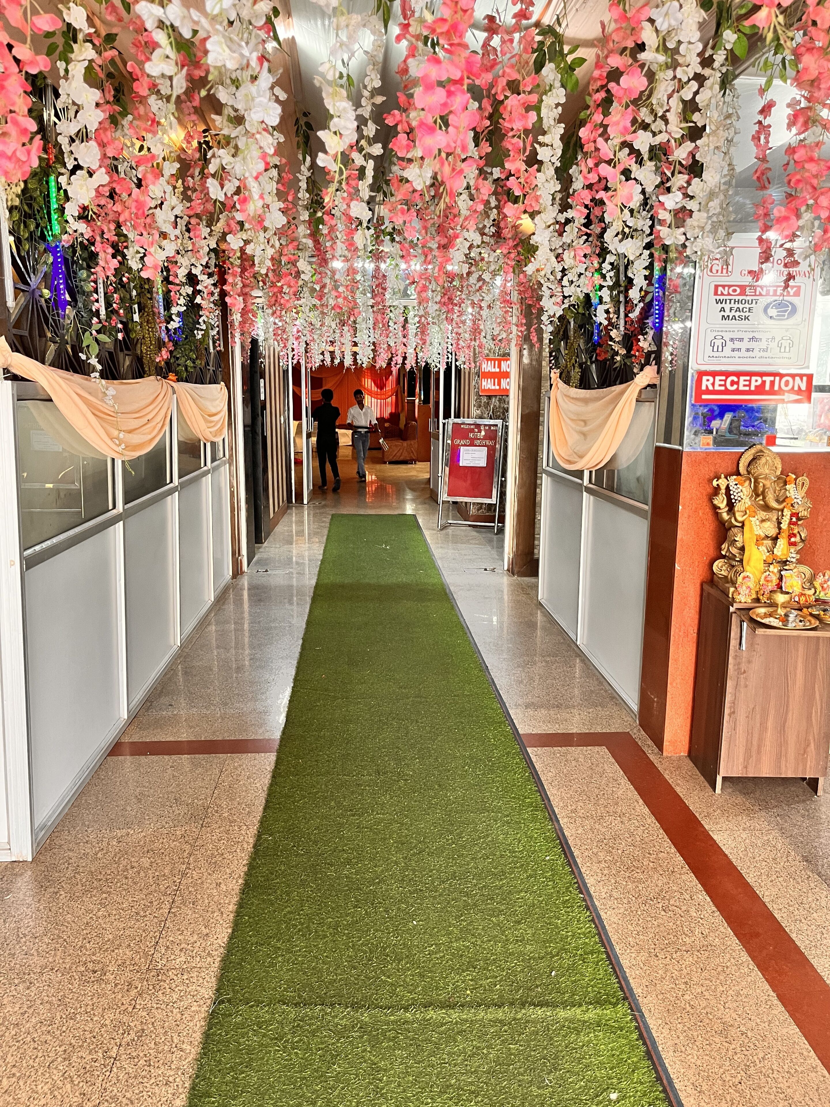 A hotel reception area with a green carpet, decorative hanging flowers, and a reception desk.