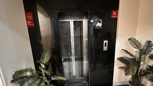 A hallway with a glass elevator door, potted plants, and a tiled floor. - HOTEL GRAND HIGHWAY (Faridabad)