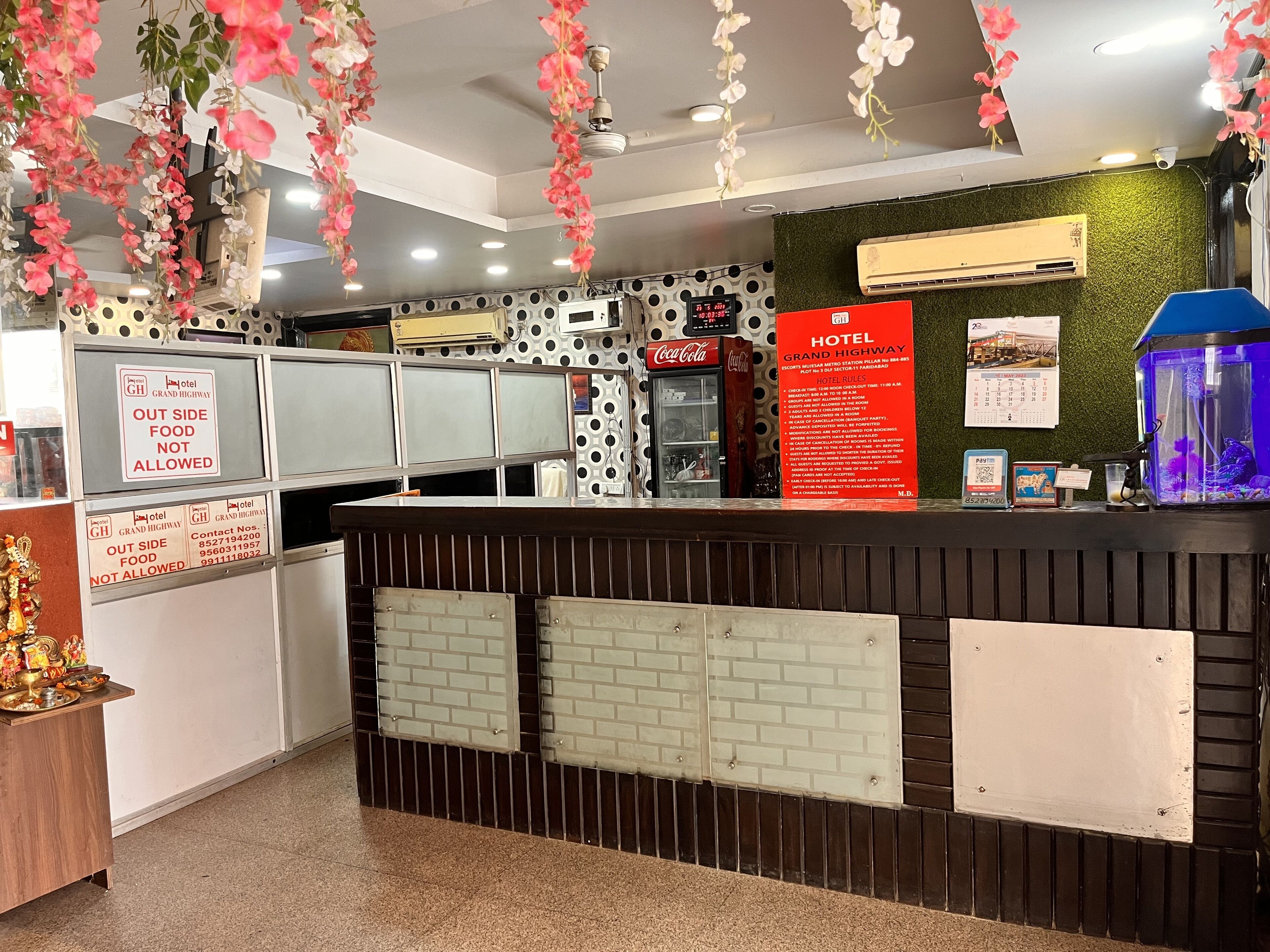 A hotel reception area with a modern design, including a reception desk, a Coca-Cola refrigerator, and a digital clock.