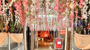 A hotel lobby with a green carpet, hanging floral decorations, and a red sign indicating hall numbers. - HOTEL GRAND HIGHWAY (Faridabad)