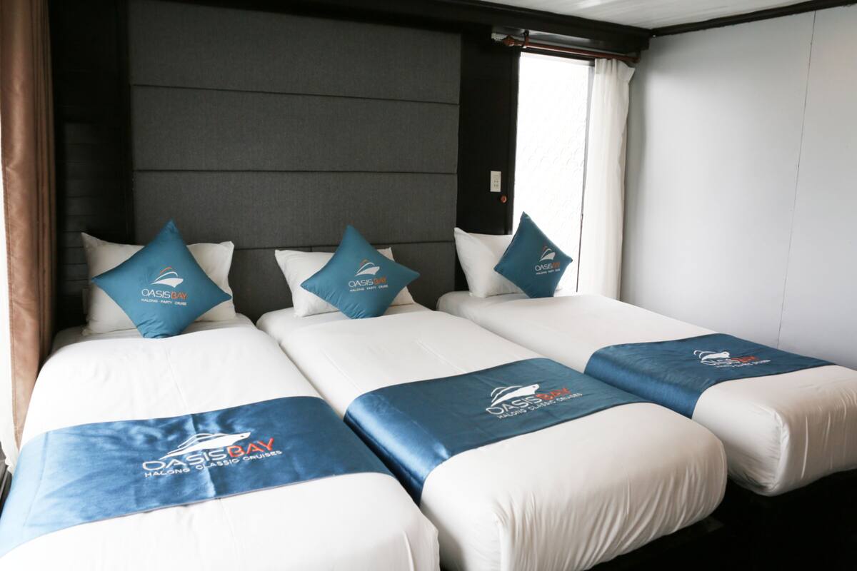 A hotel room with three beds, each with a blue Oasis Bay branded bedspread.