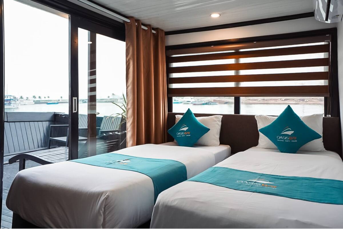 A hotel room with two beds, a balcony with a view of the water, and a window with blinds.