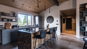 A modern kitchen with a large island, bar stools, and a wooden ceiling.