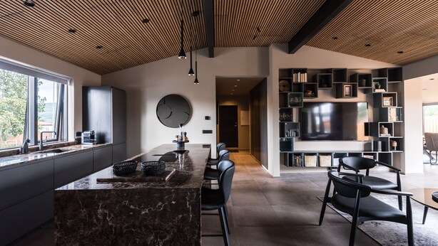 A modern kitchen with a marble island, black chairs, and a large TV in the dining area.