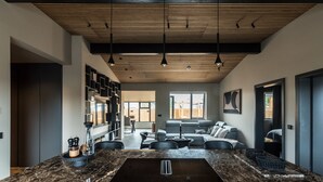 A modern kitchen with a built-in island, overhead wooden beams, and a dining area with a sofa and chairs.