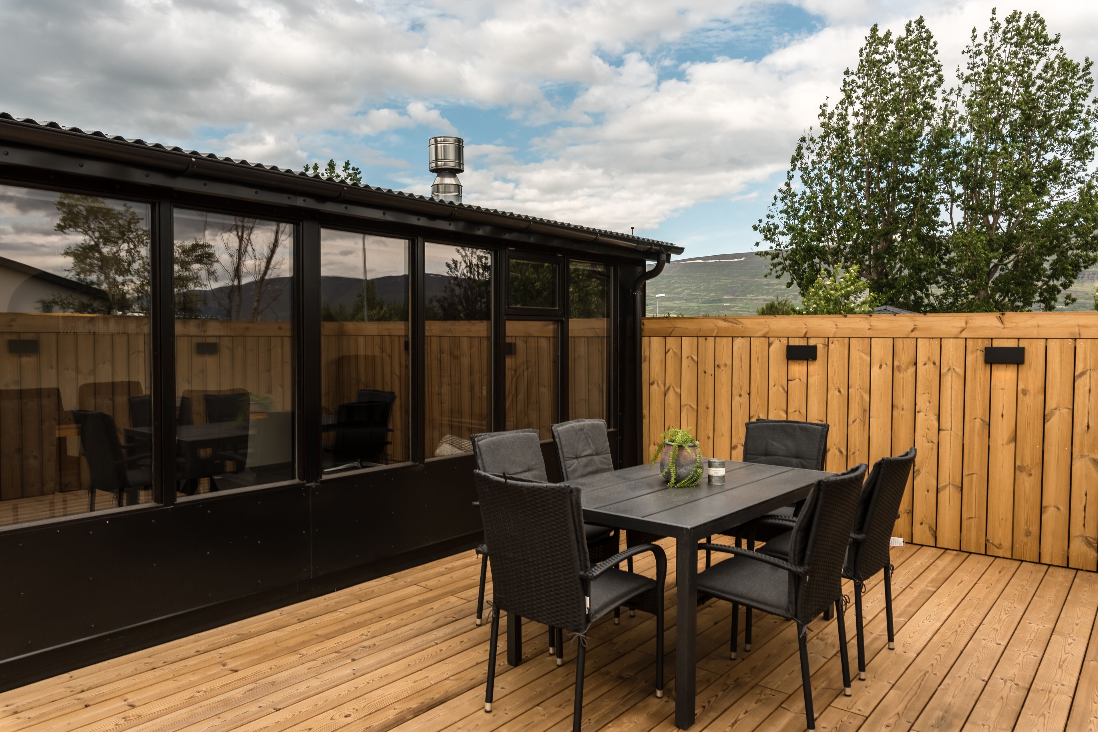 An outdoor deck with a table and chairs, a wooden fence, and a view of the landscape.