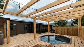 A wooden deck with a hot tub, string lights, and a pergola.