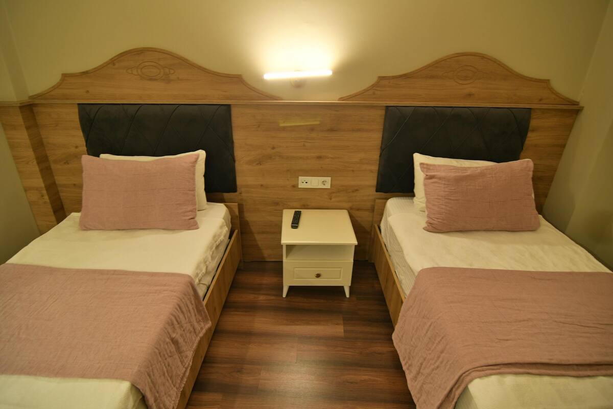 A room with two beds, each with a headboard, a nightstand, and a remote control on the nightstand.