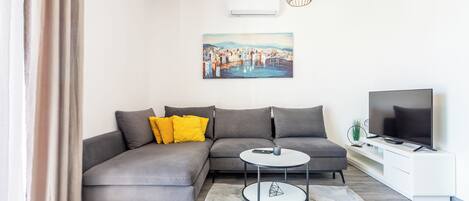 A modern living room with a grey sofa, a round coffee table, a flat-screen TV, and a painting on the wall.