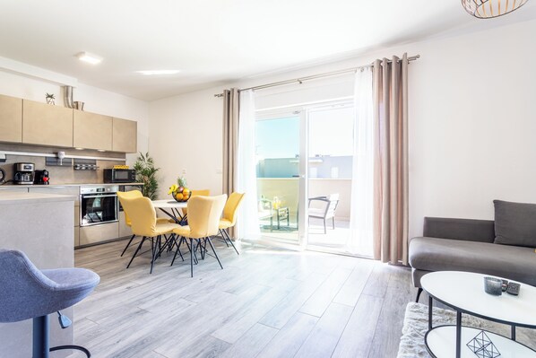 A modern kitchen with a dining area, a sofa, and a balcony with curtains.