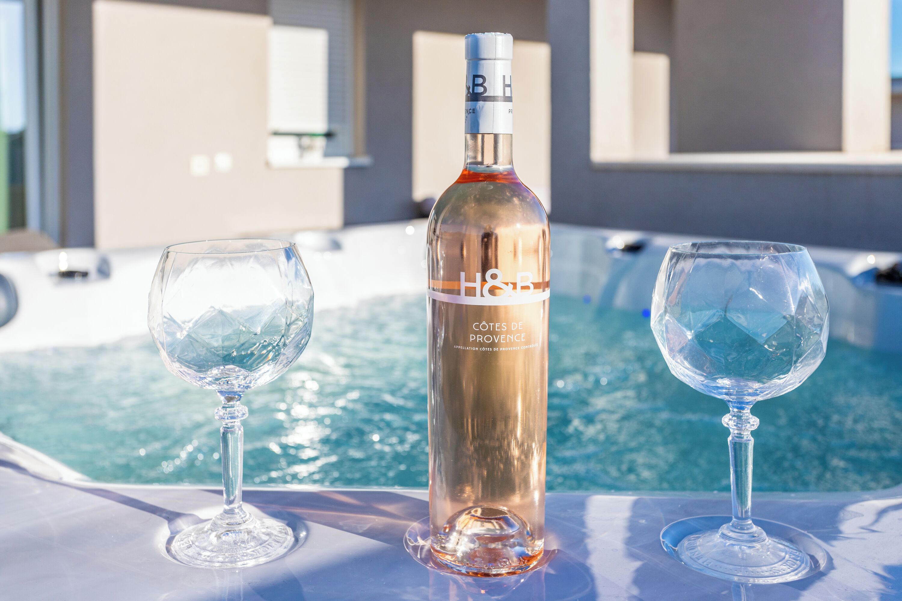 Eine Flasche H&B Côtes de Provence Wein und zwei leere Weingläser auf einem Tisch am Pool.