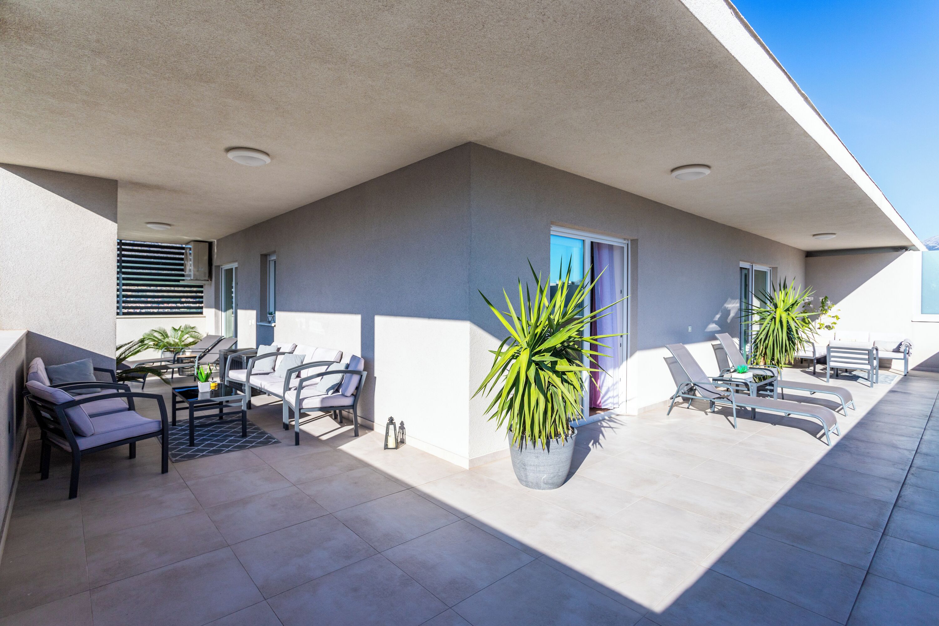 Un patio exterior moderno con una pared gris, una planta en maceta y varios sillones de relax.