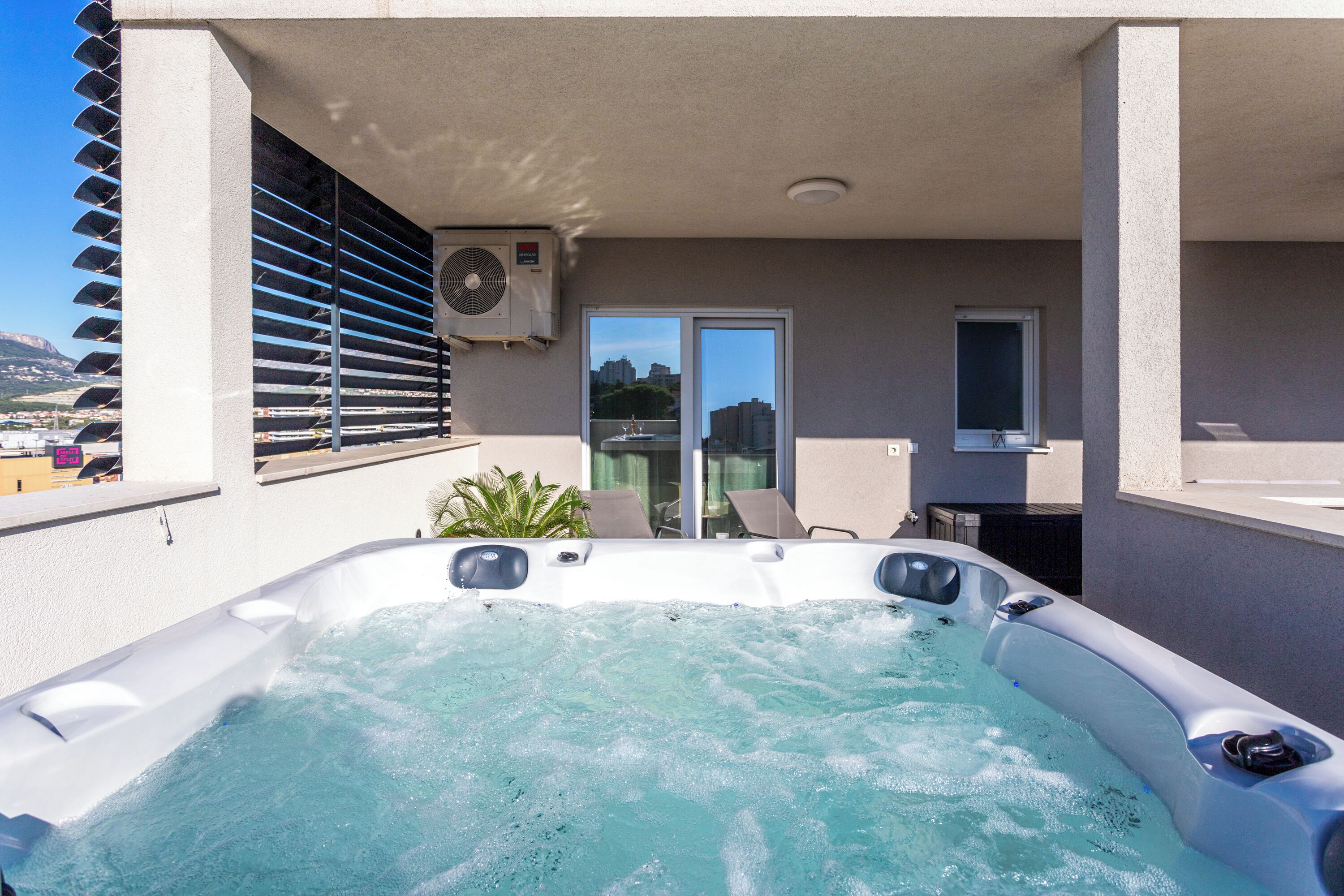 Un jacuzzi en un balcón con vistas a la ciudad, una ventana y un equipo de aire acondicionado.