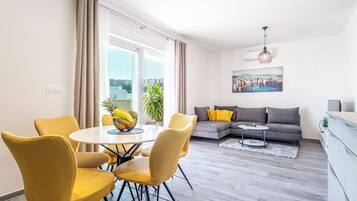 Una sala de estar moderna con zona de comedor, un sofá gris con cojines amarillos y un cuadro en la pared.