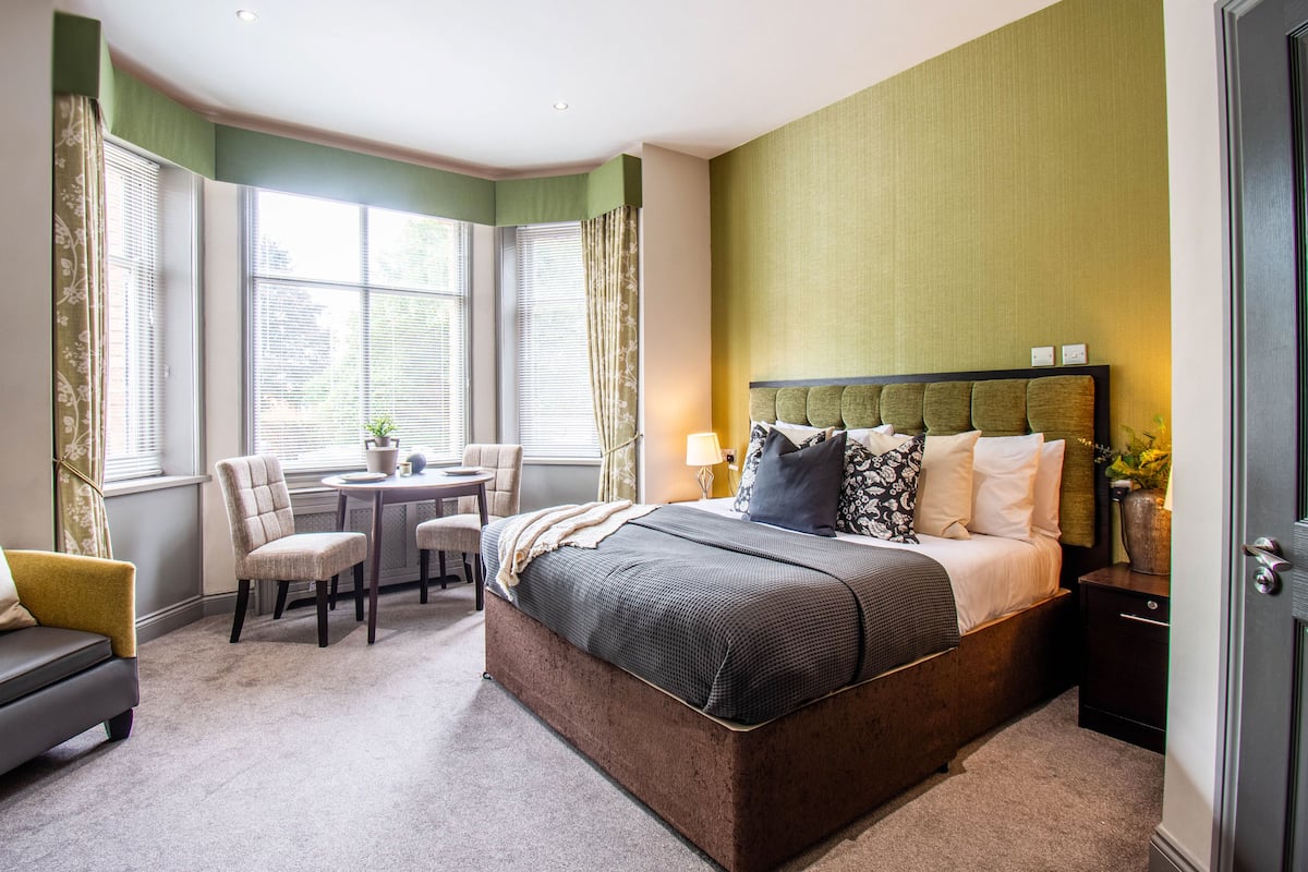 A hotel room with a large bed, a desk, two chairs, and a sofa.