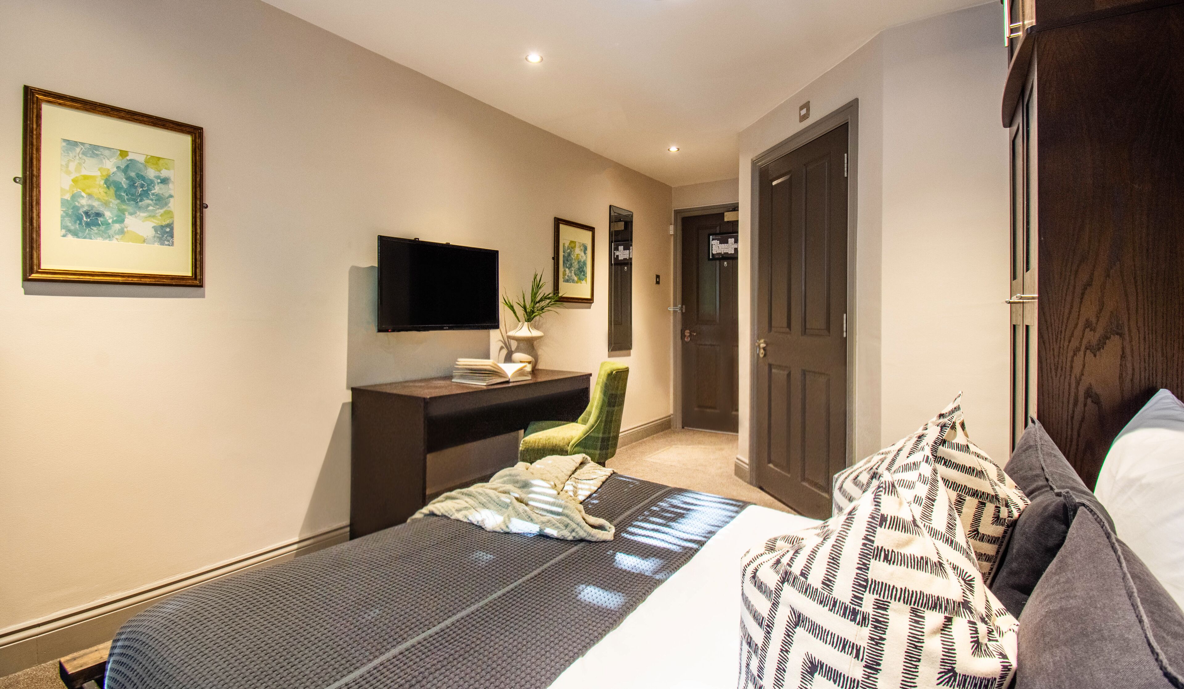 Una habitación de hotel con cama, escritorio, silla, televisor y puerta.
